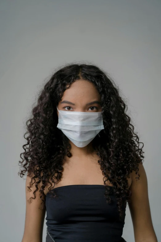 a woman wearing a surgical mask stands in front of a wall
