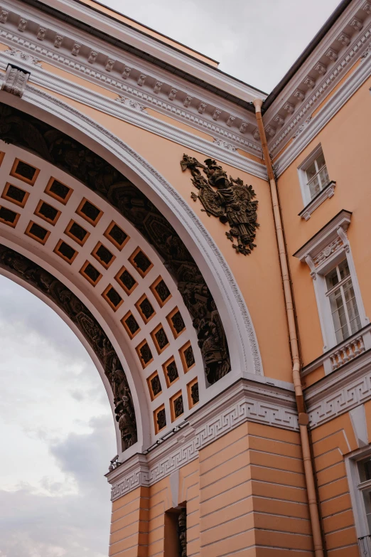 an arch over looking the sky, in front of a large orange building