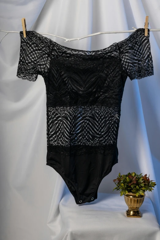 a black bodysuit with an off shoulder and black straps, hanging on a string by a potted plant