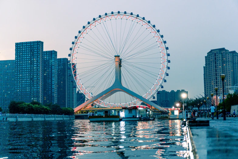 a large ferris wheel sitting over a river in the middle of a city