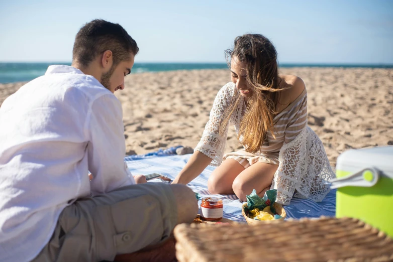 the couple are sitting on the beach and having a picnic