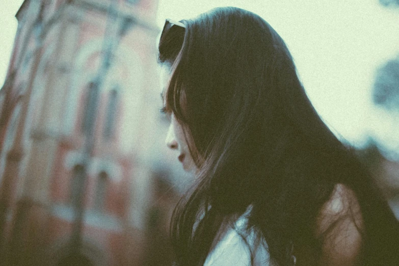 a person with dark hair and sunglasses in front of a building