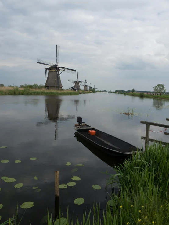 a small boat sits in the water in front of the windmills