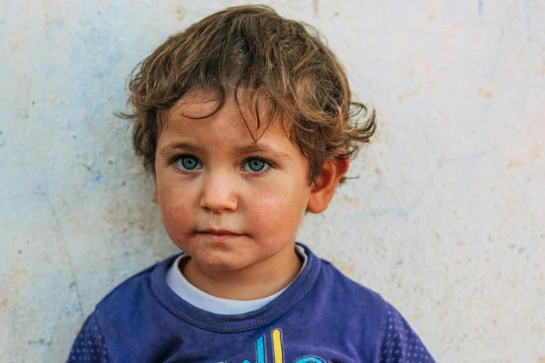 a little boy standing by a wall with his eyes wide open