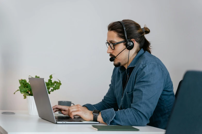 a man sitting at a desk in front of a laptop computer and wearing a headset