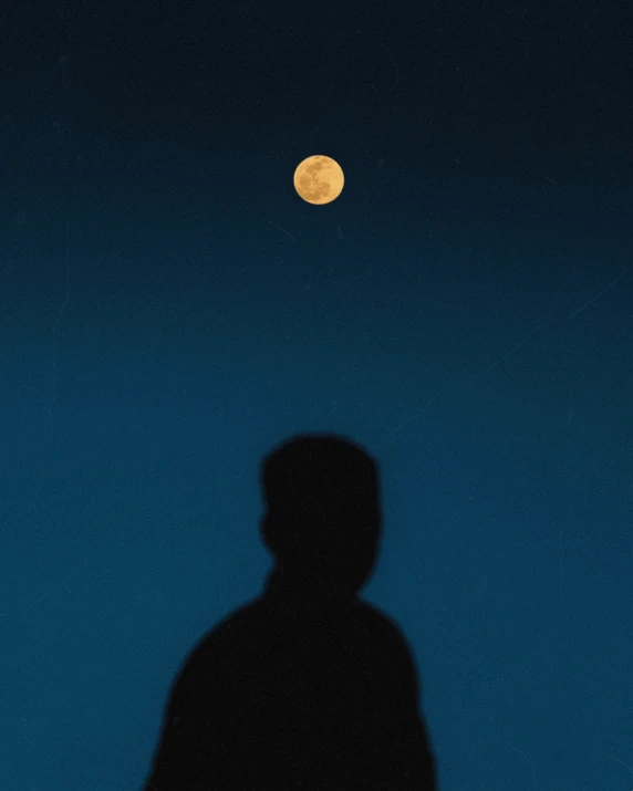 a silhouetted man against a blue sky with the moon in the distance