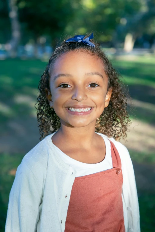 a little girl wearing an orange shirt smiles at the camera