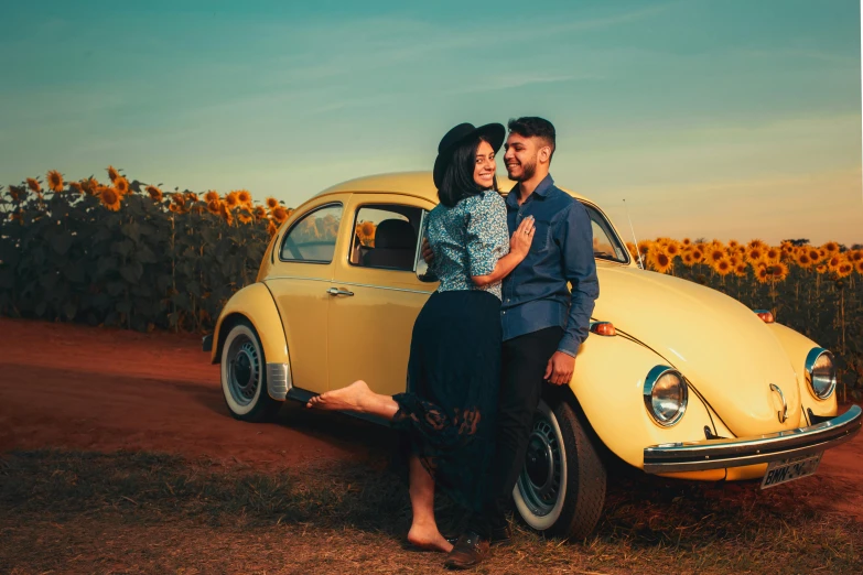 a man and a woman standing in front of a vw beetle parked in a field with sunflowers