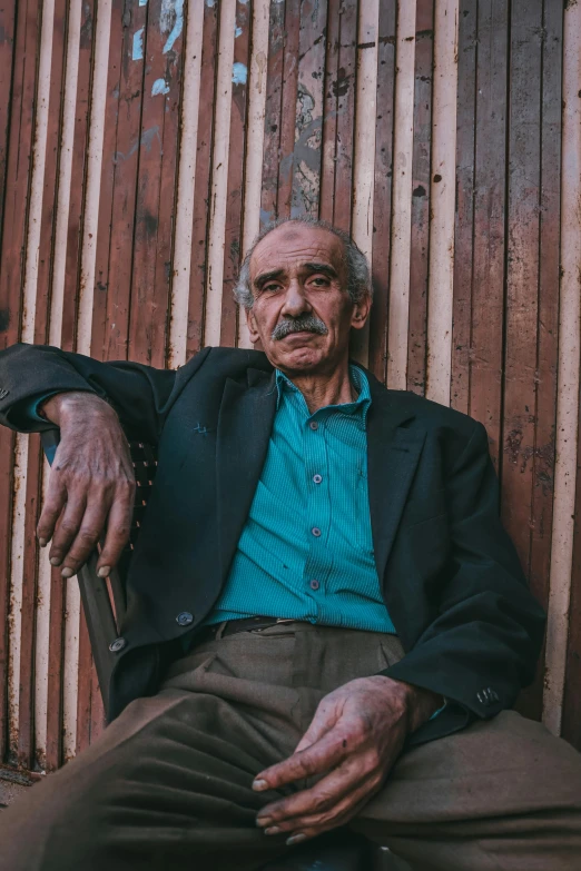 an old man in suit and tie sitting next to a wooden fence