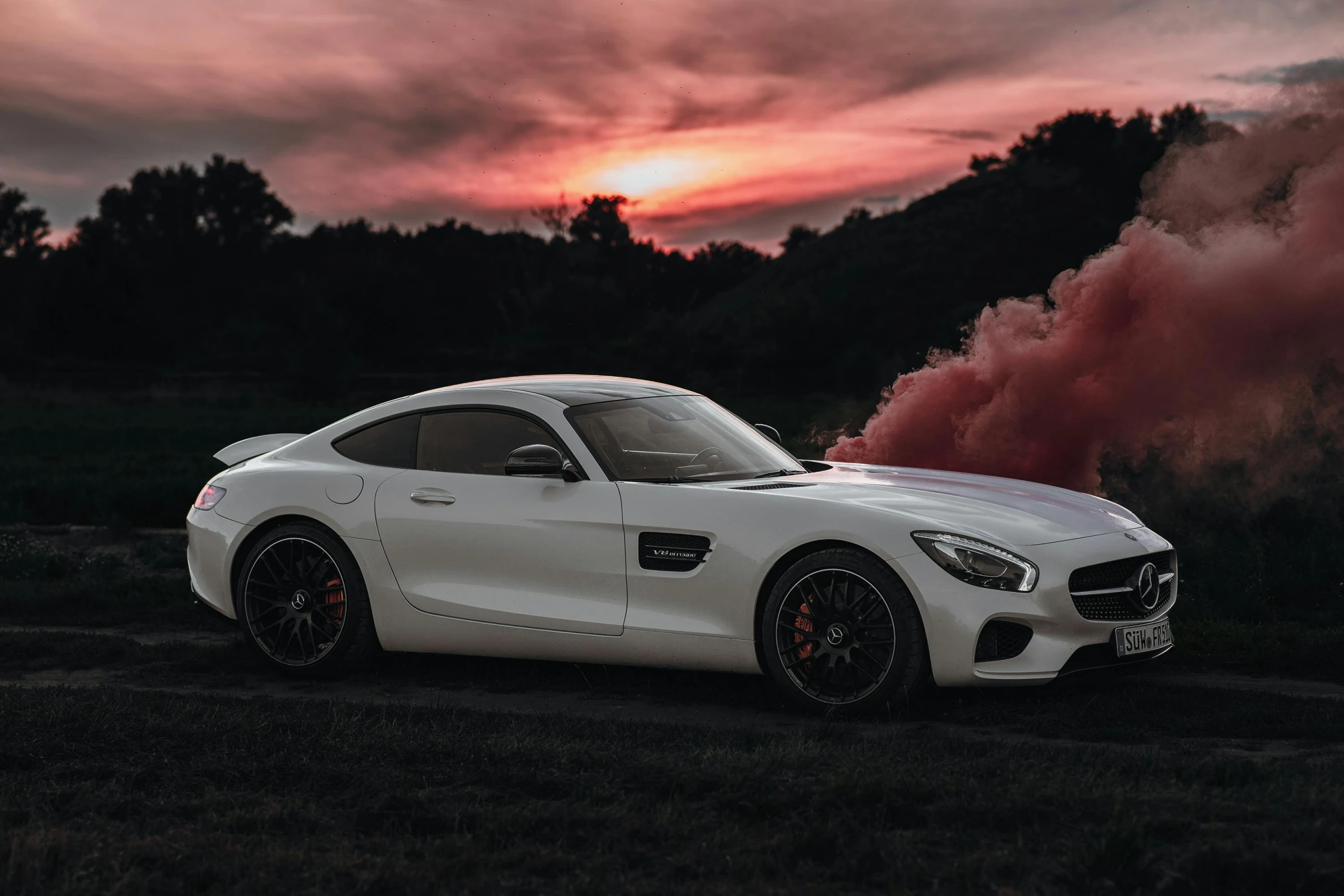 white mercedes sports car in a field with trees and a pink cloud