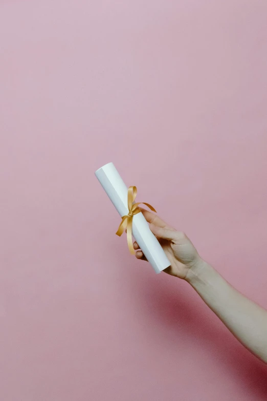 woman's hand holding a white paper tube with golden bow