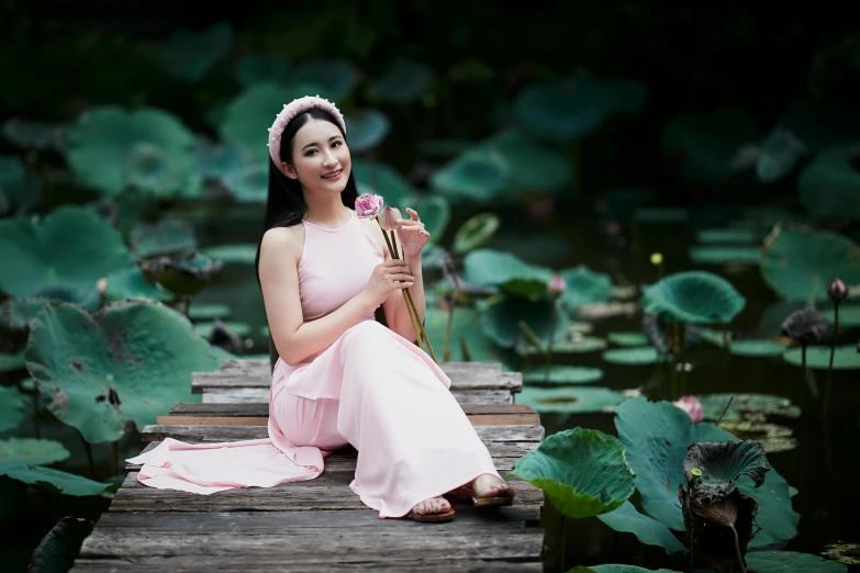 a woman is sitting on a dock holding a rose