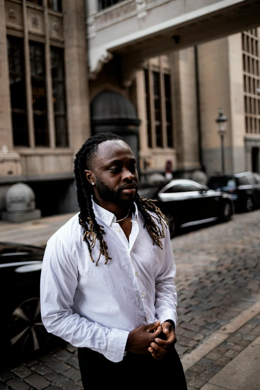 a man with dread locks and white shirt in front of a black car