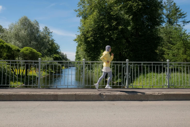 a person runs beside a gate as a bridge crosses a river