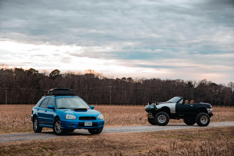 two cars driving along a gravel road next to an open field