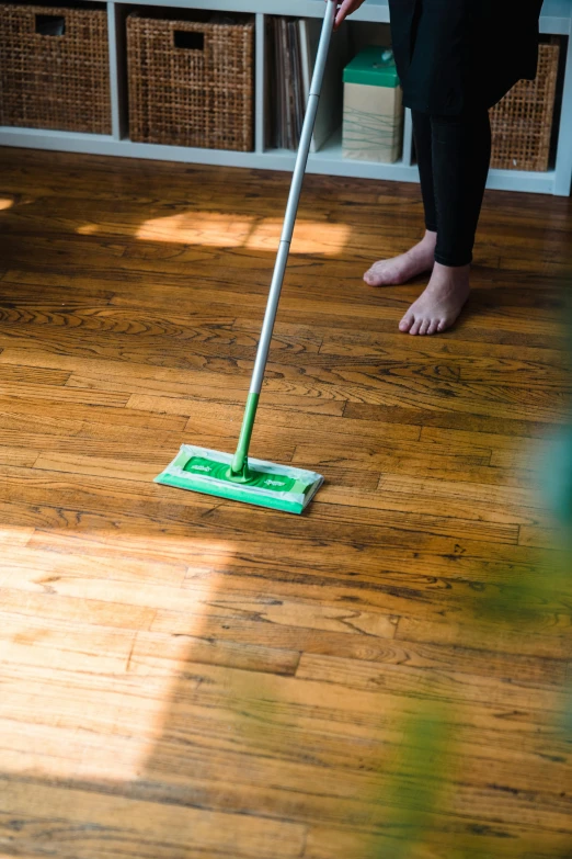 a person with feet up on a wooden floor with a broom