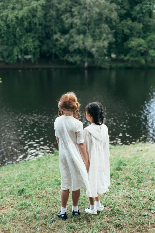 two children standing in front of a lake in an old fashion clothing