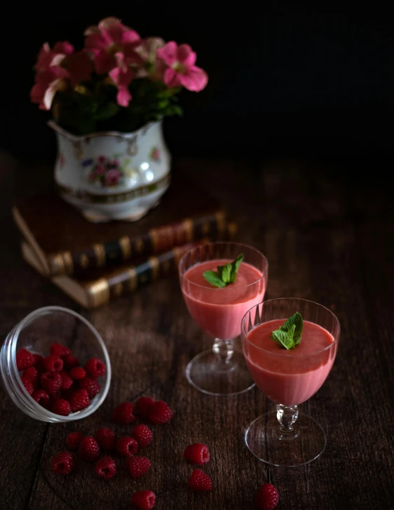 three wine glasses with pinkish red liquid sitting next to flowers