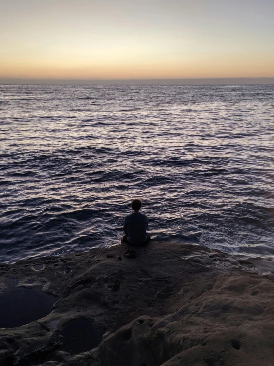 a person sits on some rocks at the ocean