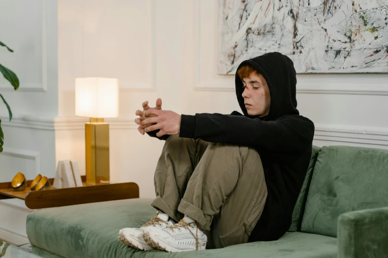 a young man sitting on a green couch with his hands crossed