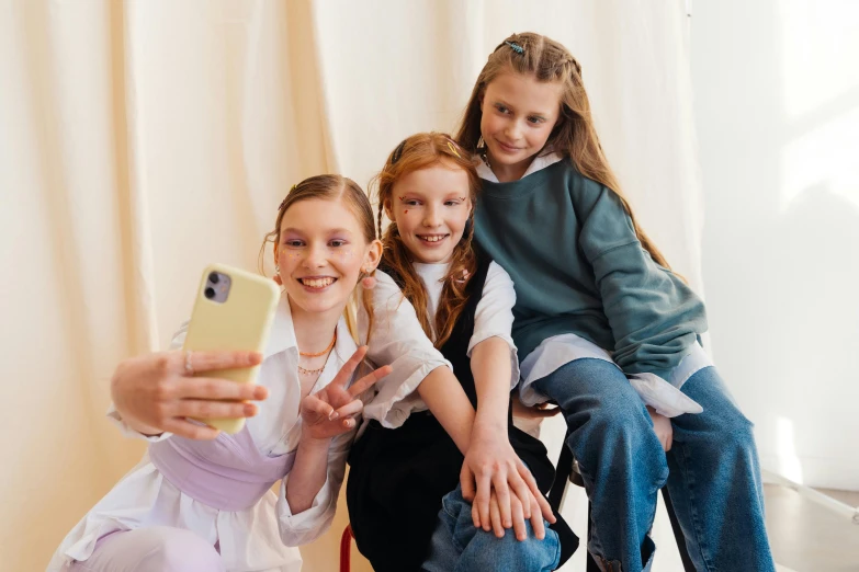 two girls sitting on a chair taking a selfie with their mother