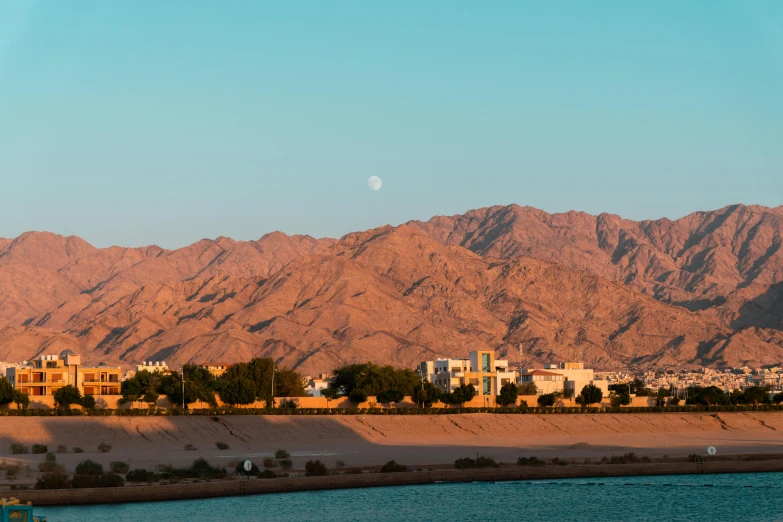 a view from the banks of a river that is running past a city in front of mountains