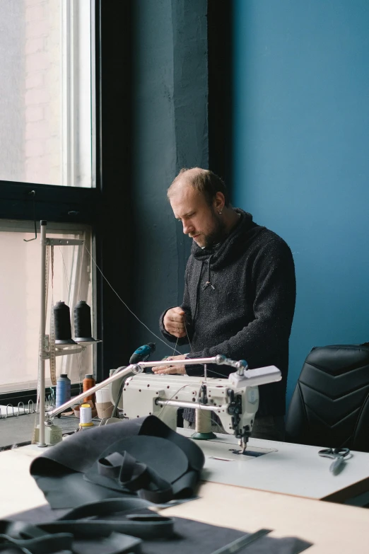 man working with sewing machine in front of window