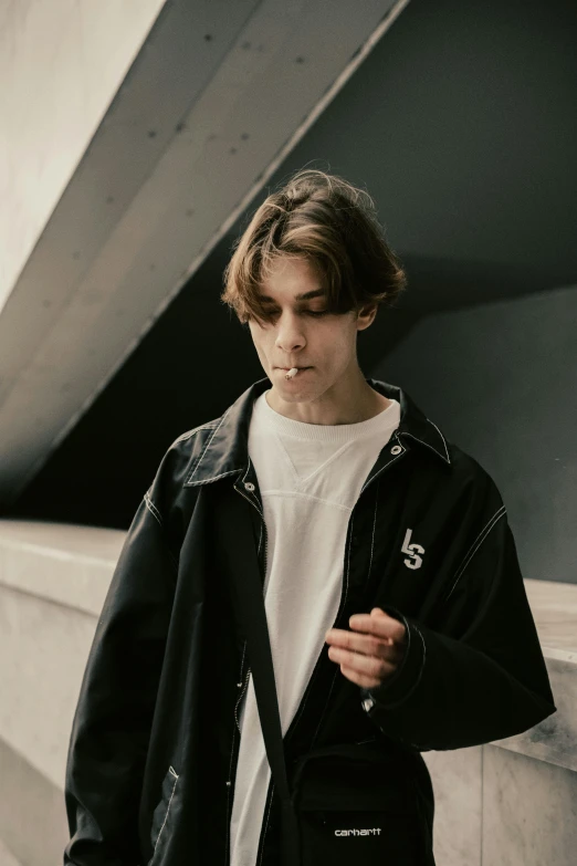 man standing by a wall, wearing a black leather jacket and white t - shirt