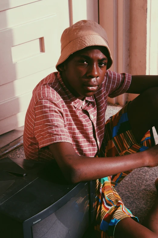 a black man in a tan hat sitting on a suitcase