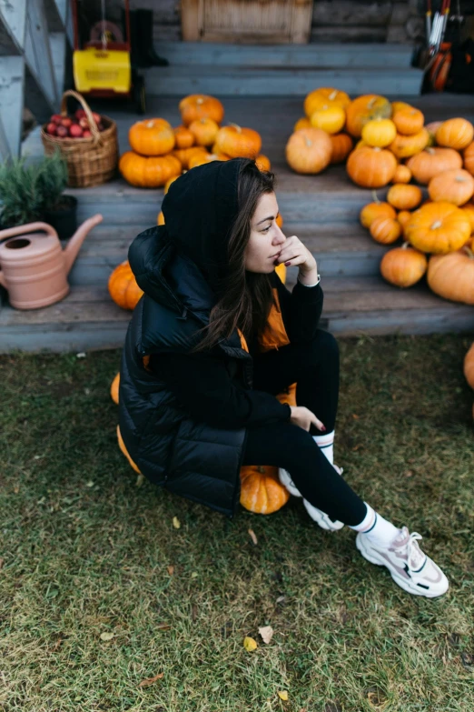 girl in black coat sitting on steps next to a garden filled with pumpkins