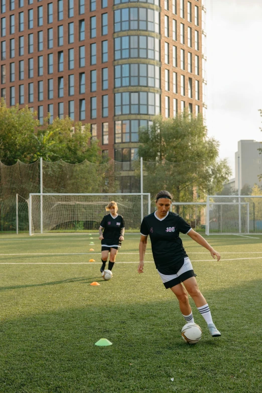 two women play soccer in front of a tall building