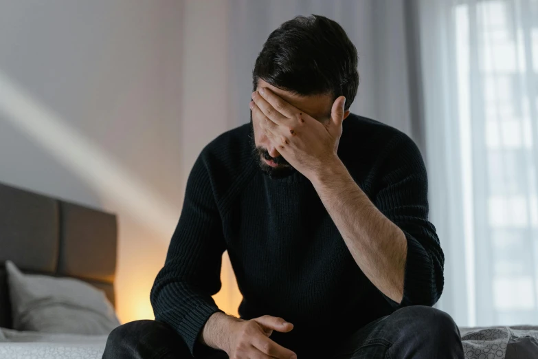 man sitting on bed covering his face with his hand