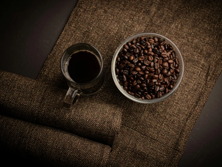 a cup of coffee and some beans are placed next to a pair of cloth