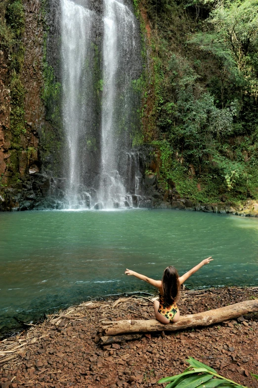 a woman sits at the edge of a waterfall