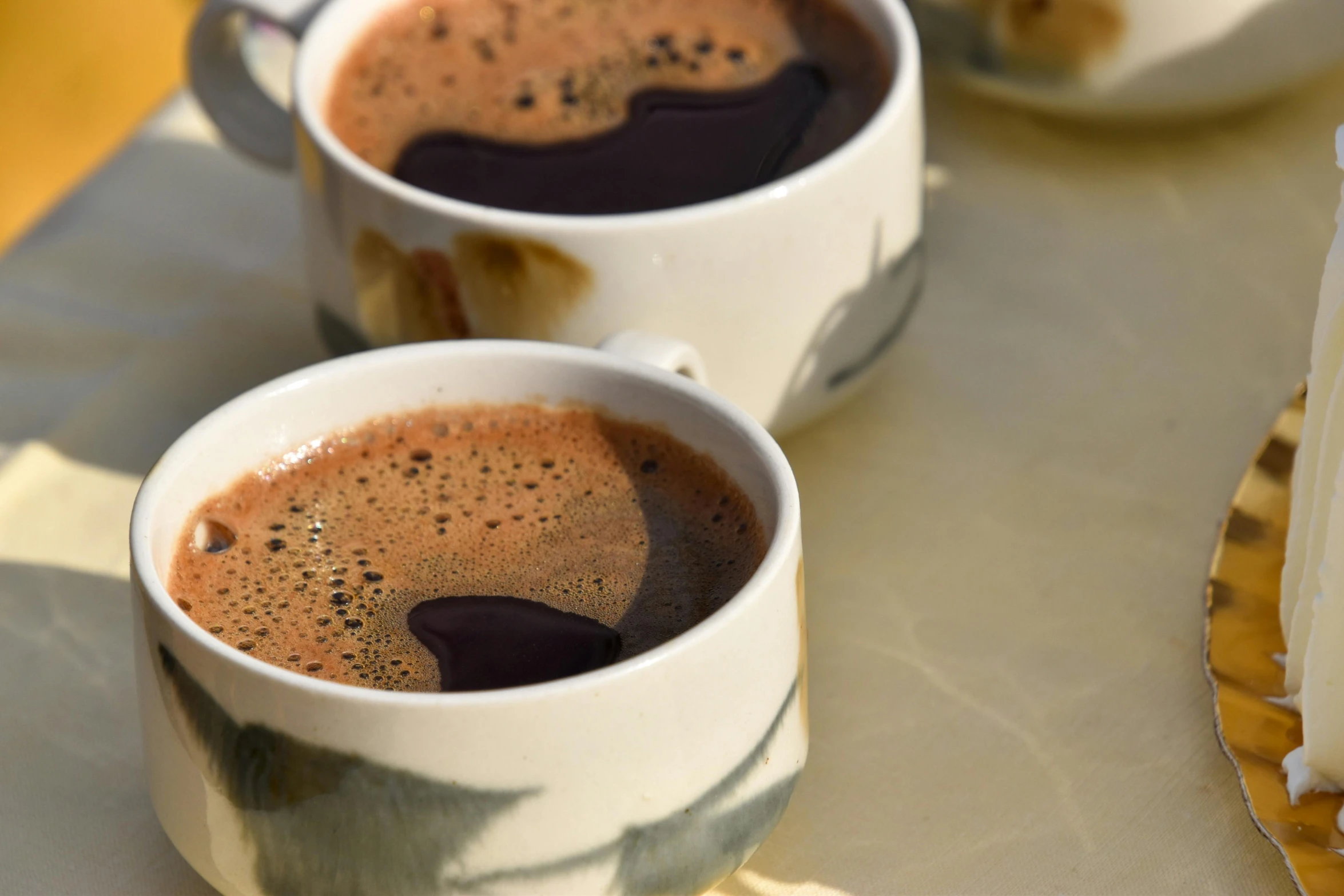 two coffee cups on a table with cake in the background