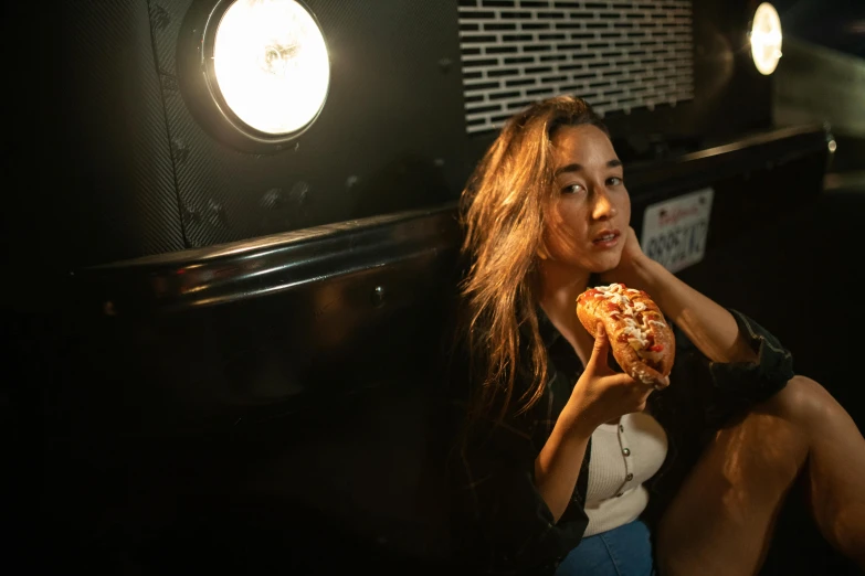 the woman sitting in the dark eats a slice of pizza