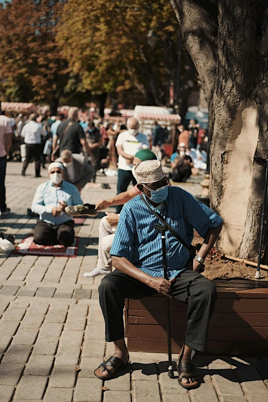 an elderly man sits in a suitcase and listens to music while surrounded by people