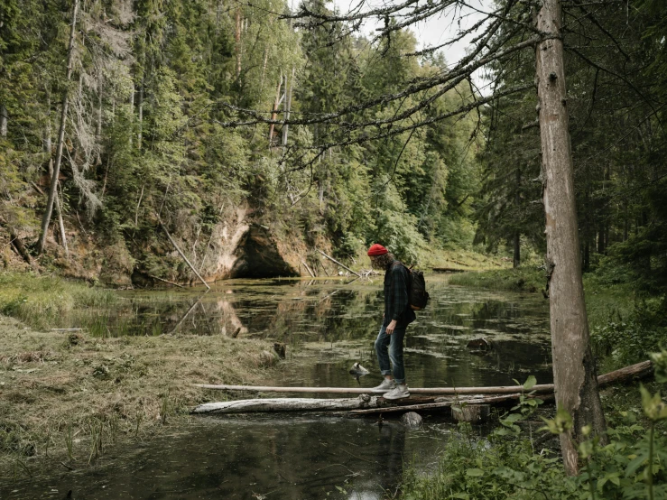 a man stands on a log over a creek in the woods