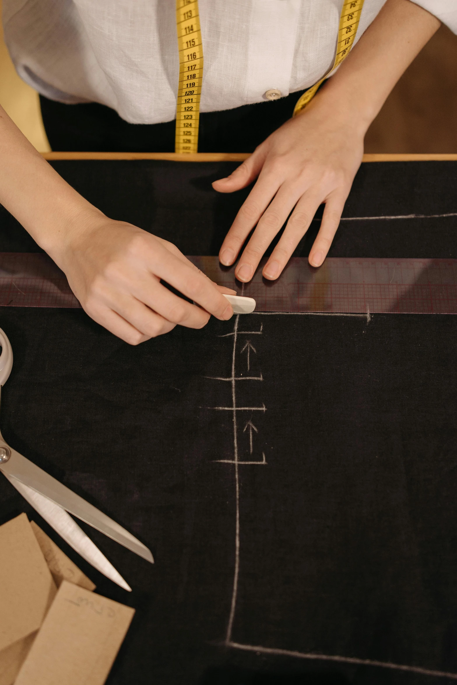 two hands on the edge of a black cloth  fabric with a pair of scissors