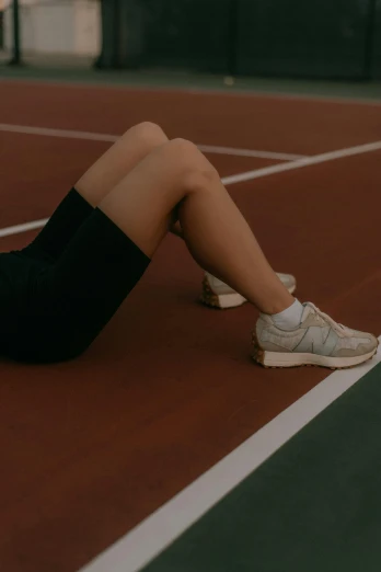 a girl sitting on a tennis court with her legs up