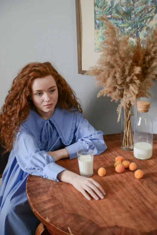 a woman sitting at a table near a vase with oranges