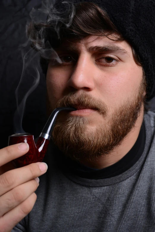 a man wearing a beanie holds a pipe in front of his face