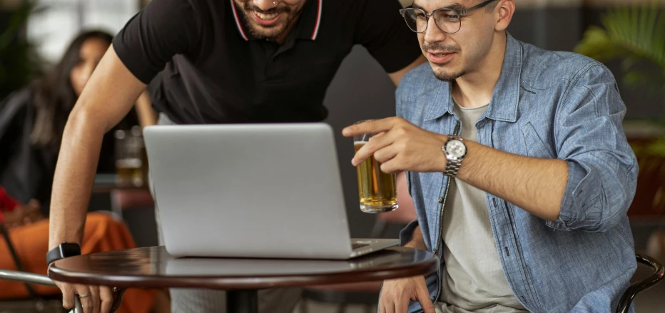 a man and woman sit at an outdoor table while looking at a laptop