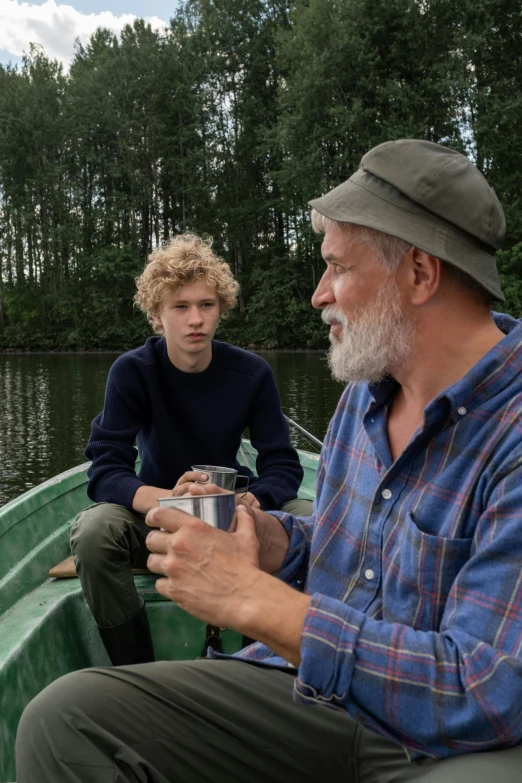 two men sitting on a boat while one holds a can of beer