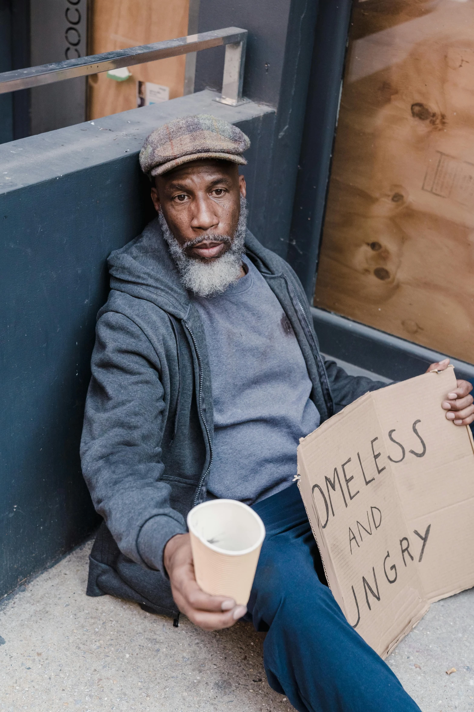 a man sitting outside holding a sign and a drink