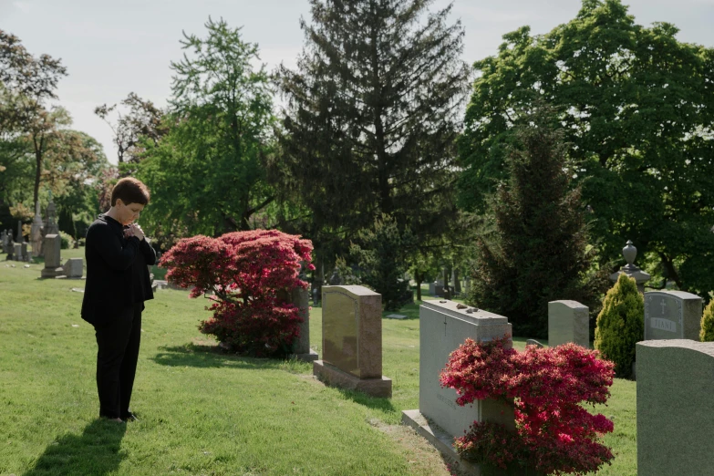 woman at grave yard on cell phone in front of flowers