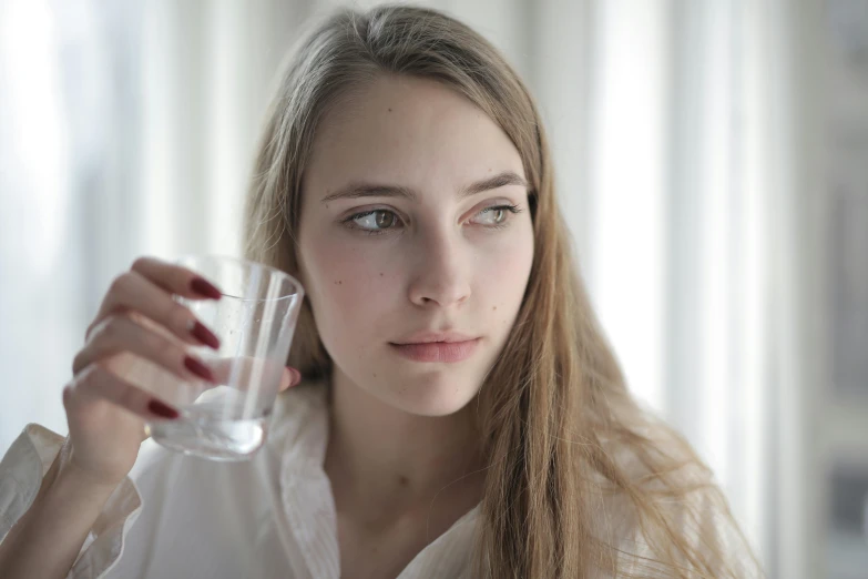 the girl is drinking from a glass near her face