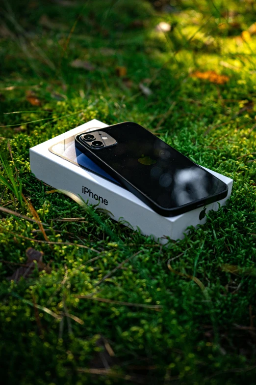 an apple phone is in the grass beside a package