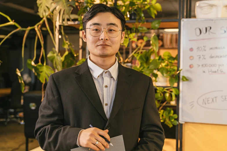 a man with glasses, a suit and a tie holds a binder in front of him