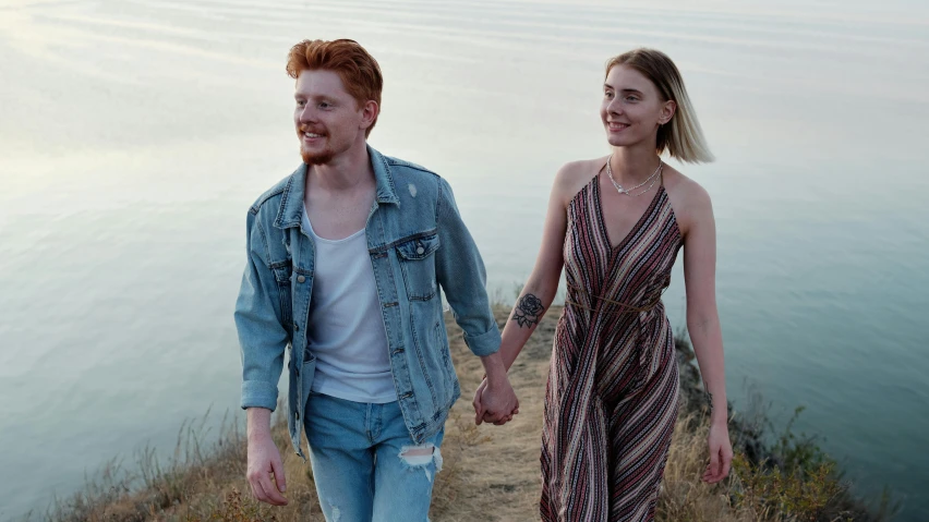 the couple are walking near water holding hands